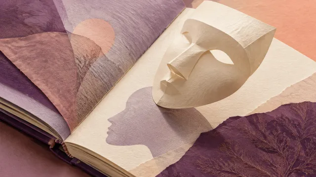 A cream paper mask rests on an open book above a purple profile, surrounded by layered paper.