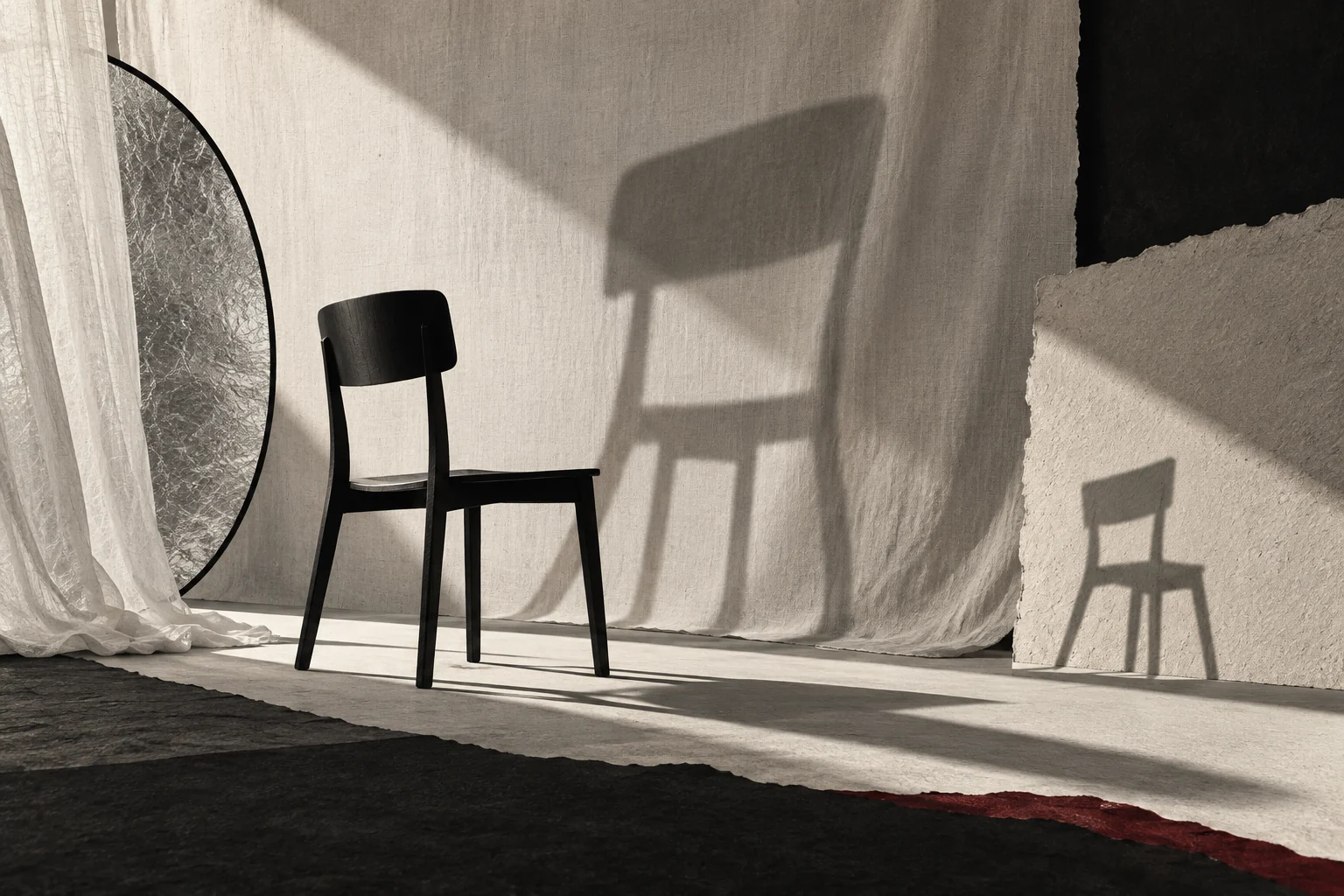 One black chair casts a broad soft shadow and a small sharp shadow across fabric and paper.