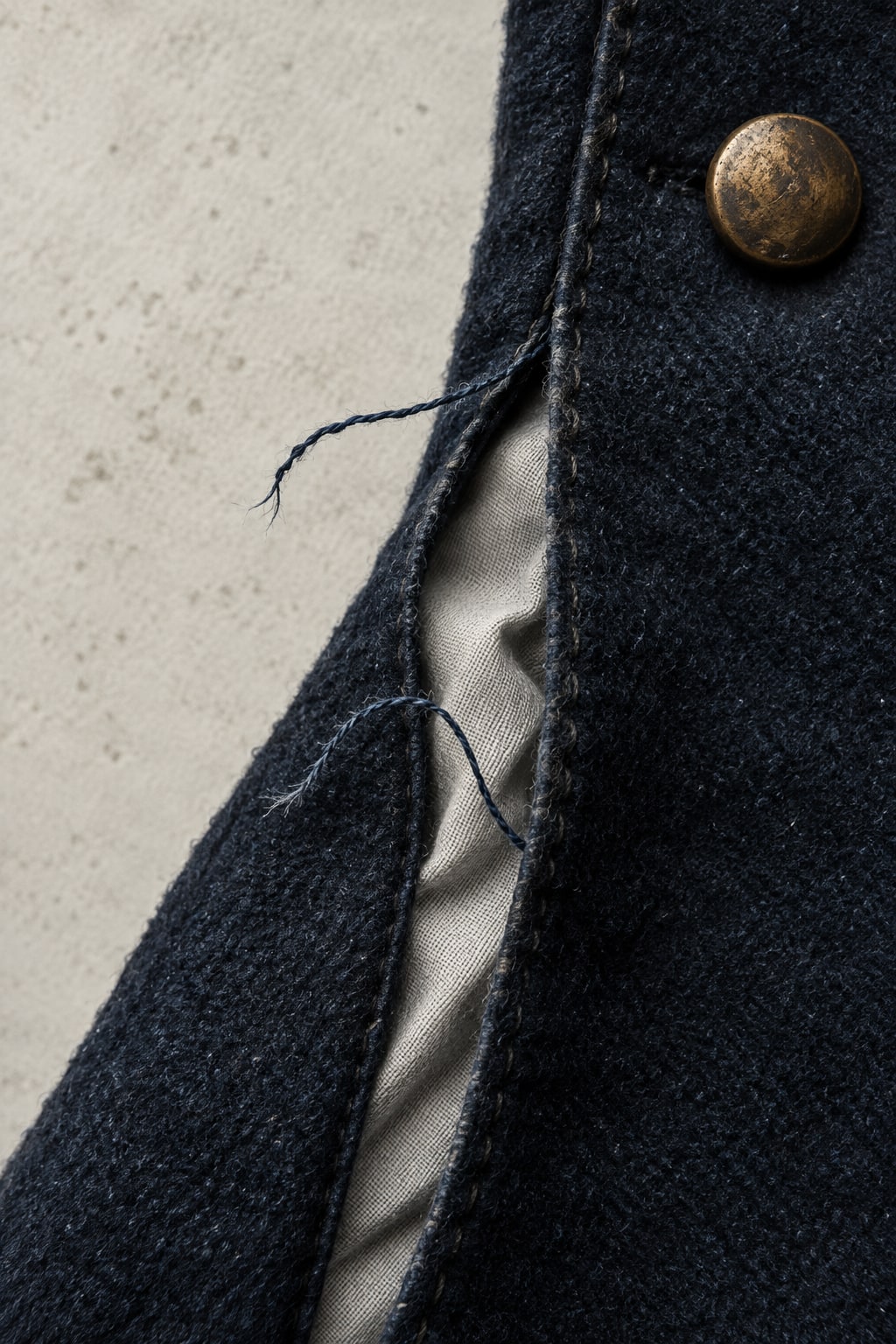 A close-up of frayed dark fabric, a brass button and a strip of white lining.